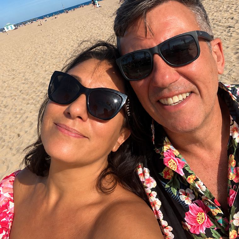 Louisa and Mark, smiling in sunglasses on a beach.